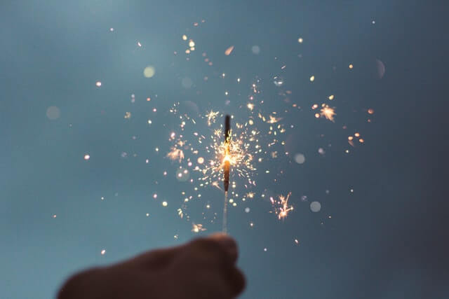 A person holding a single and lit sparkler to illustrate New Years Eve celebrations.