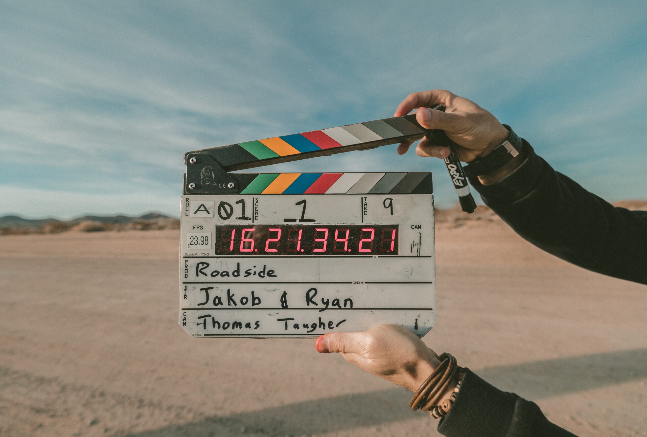 A person holding a C clapper board behind a desert background.