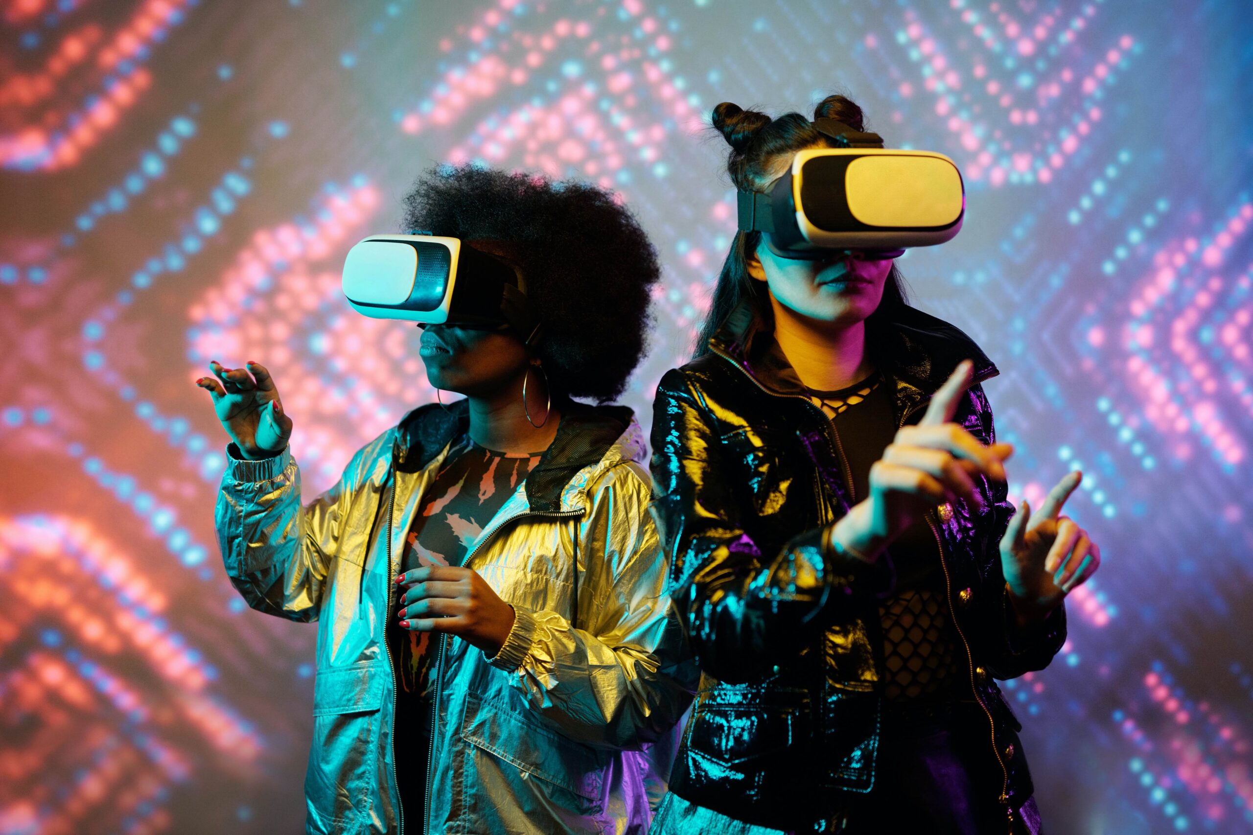 Two women wearing virtual reality googles, standing in front of a kaleidoscope background.