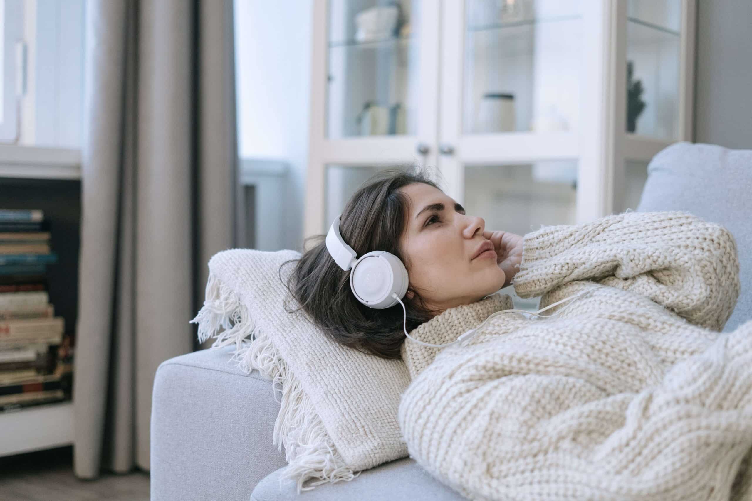A woman lying down on a sofa, wearing headphones, listening to music.